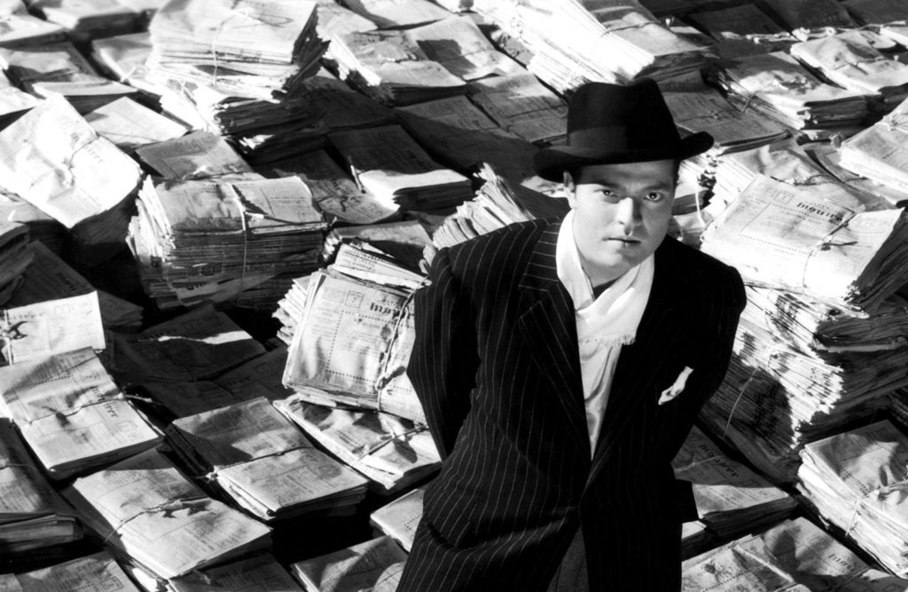 CITIZEN KANE, Orson Welles, 1941, astride stacks of newspaper